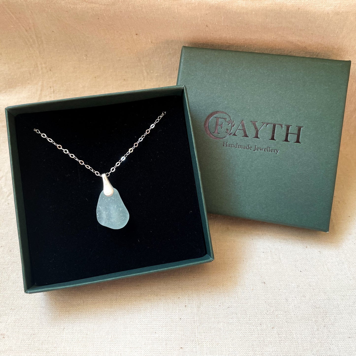 Blue sea glass necklace on silver chain in a dark green gift box with black foam insert