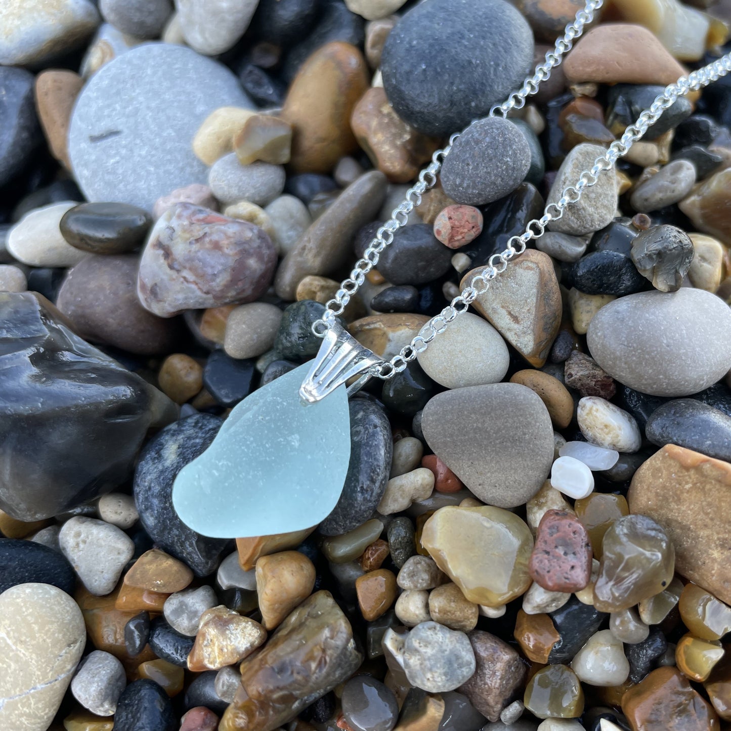 light blue seaglass necklace on top of pebbles at the beach