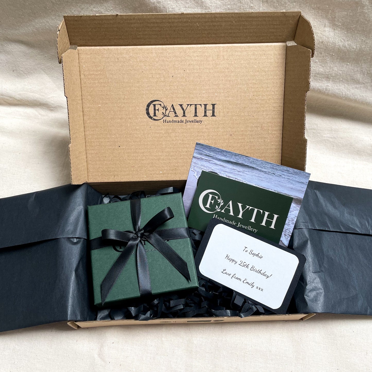 Dark green gift box with black ribbon inside a brown cardboard box with black tissue paper, business cards and note card