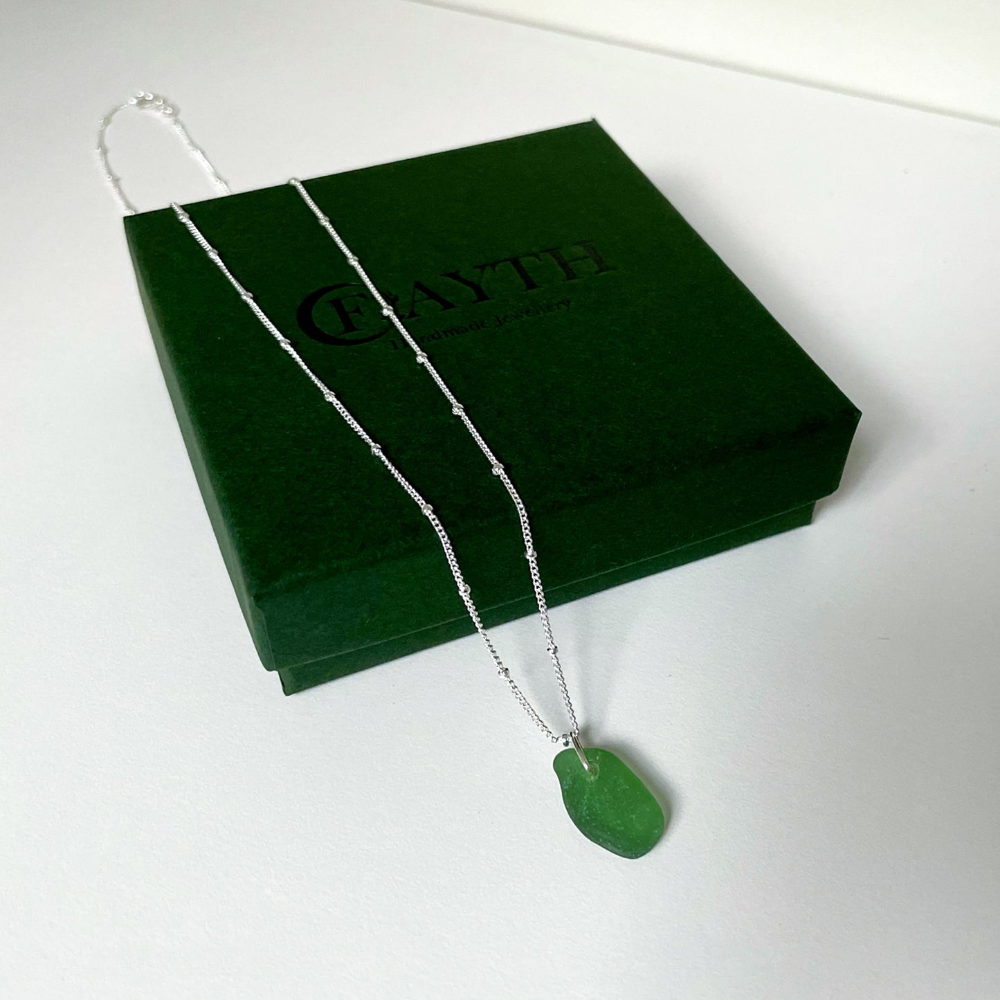 Green sea glass necklace on silver satellite chain hanging over dark green gift box