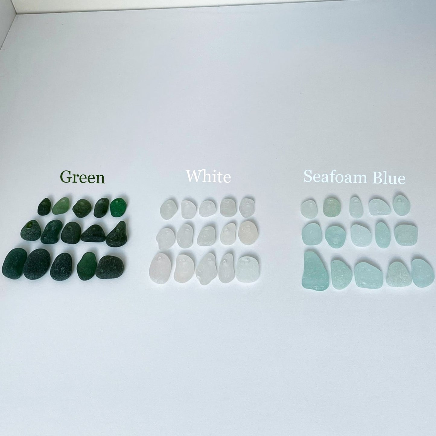 Pieces of sea glass in various sizes; on the left green sea glass, middle white sea glass and on the right light blue sea glass.