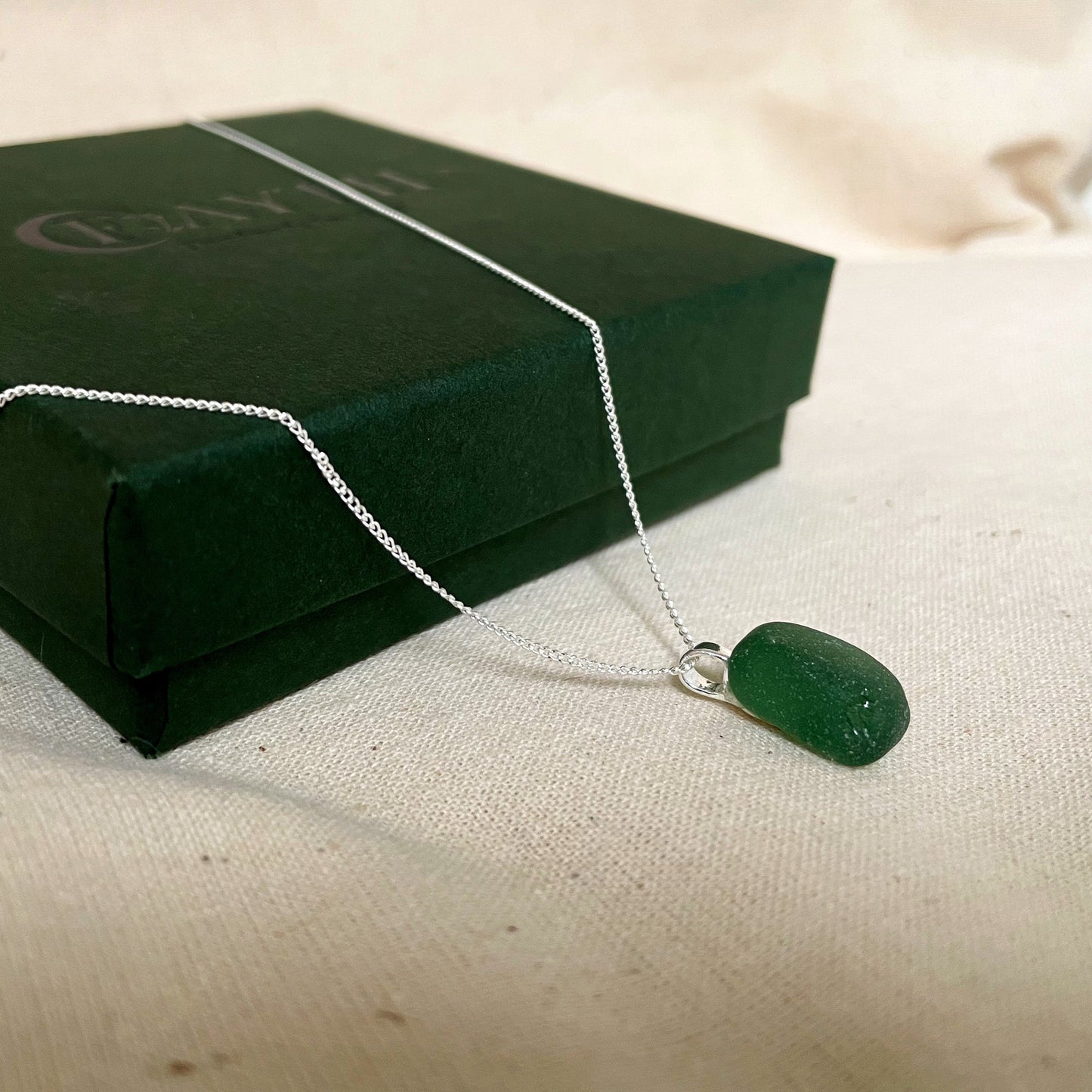 Green sea glass necklace on a sterling silver fine chain laid over a dark green gift box