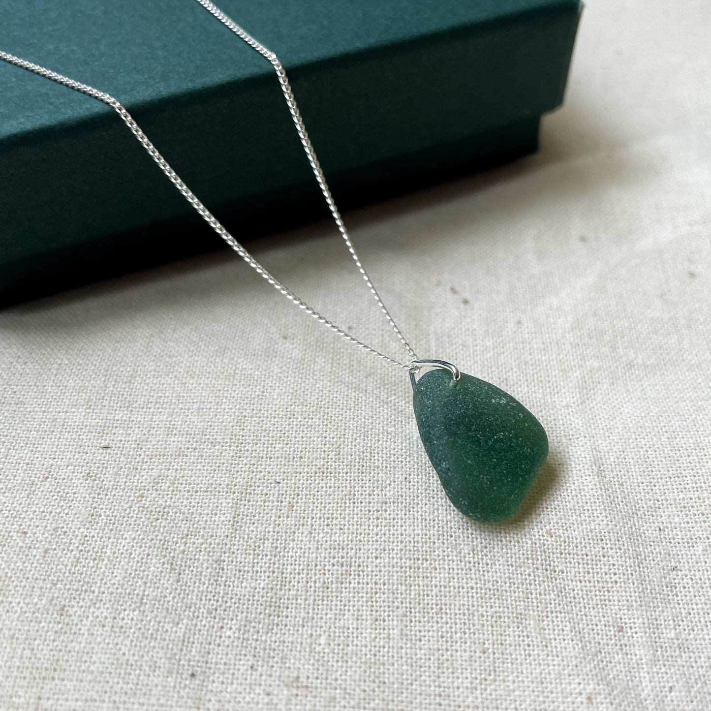 Green sea glass necklace on fine silver chain hanging over a dark green gift box