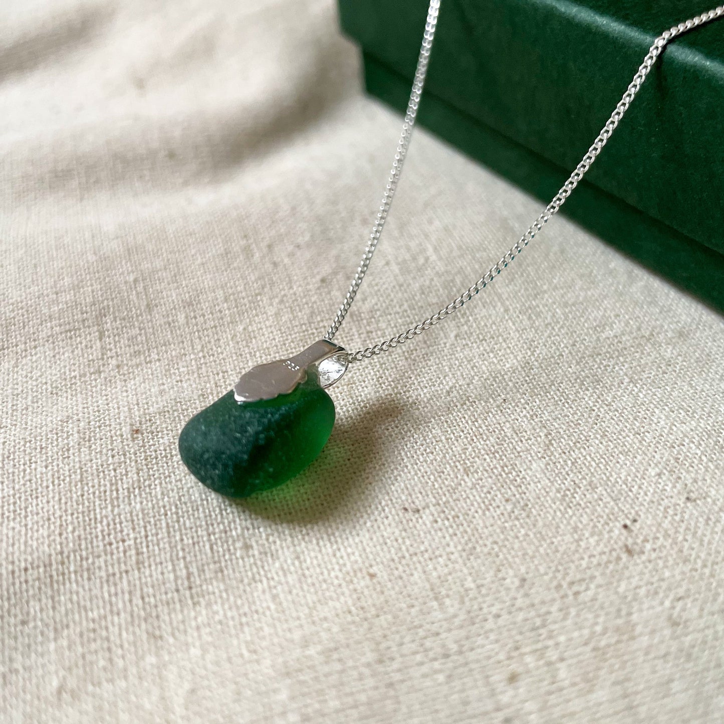 Back of Green sea glass necklace on a fine sterling silver chain laid over a dark green gift box