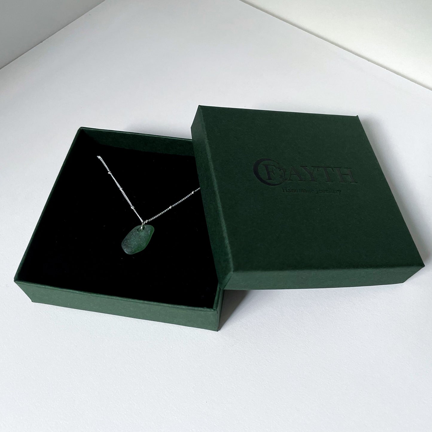 Green sea glass necklace in gift box. Gift box is dark green with black foam.