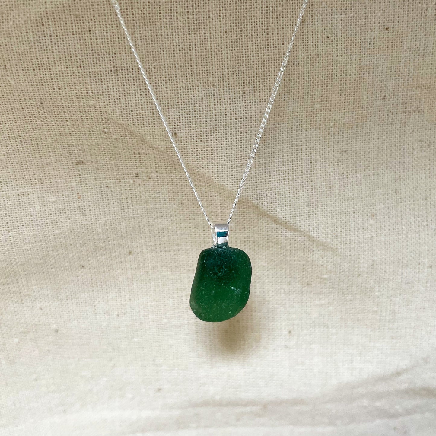 Green sea glass and sterling silver necklace hanging against a beige background