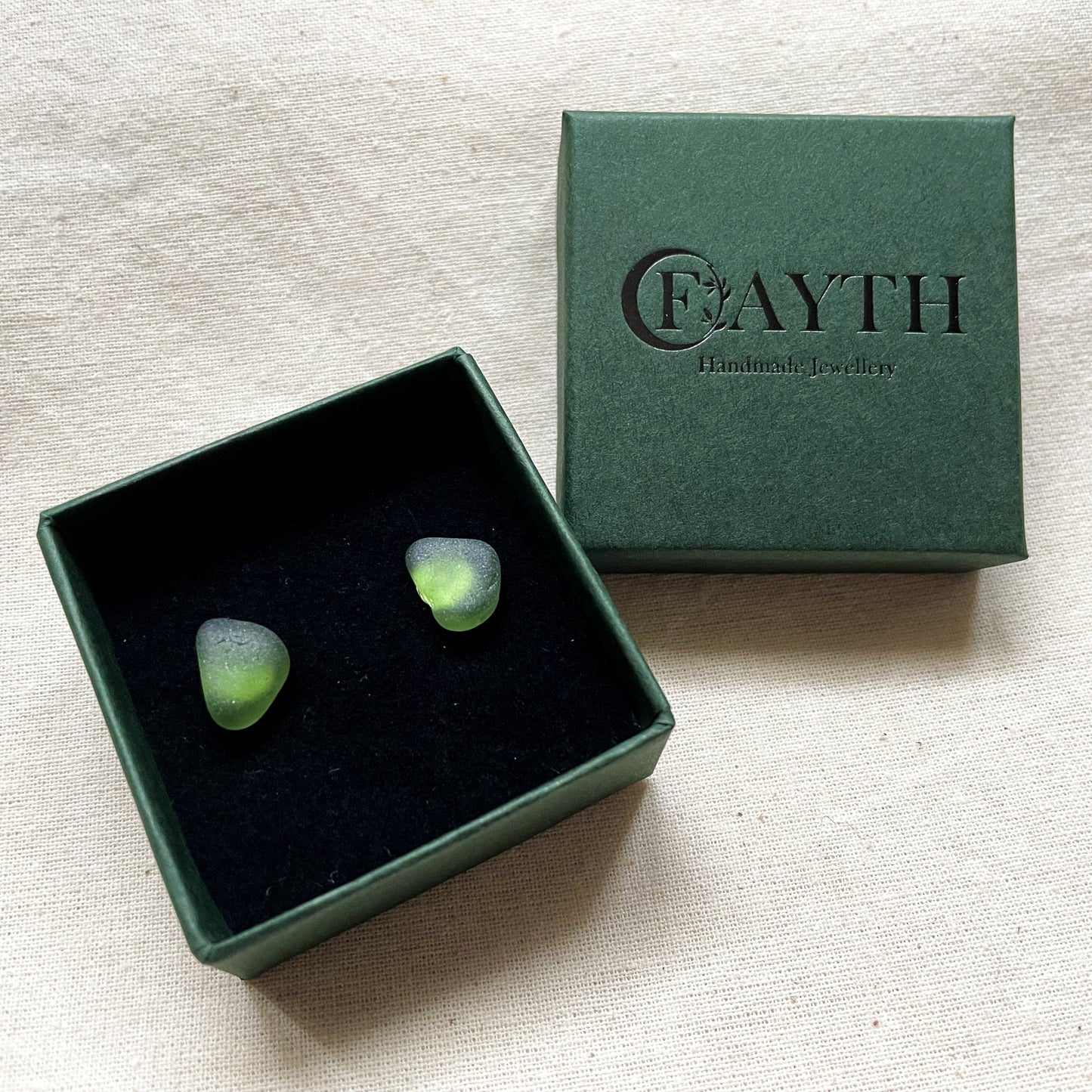 Green sea glass studs in a small dark green branded gift box with black foam inside