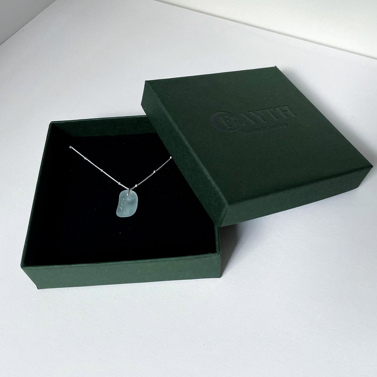 Light blue sea glass necklace on silver satellite chain in a dark green gift box with a black foam