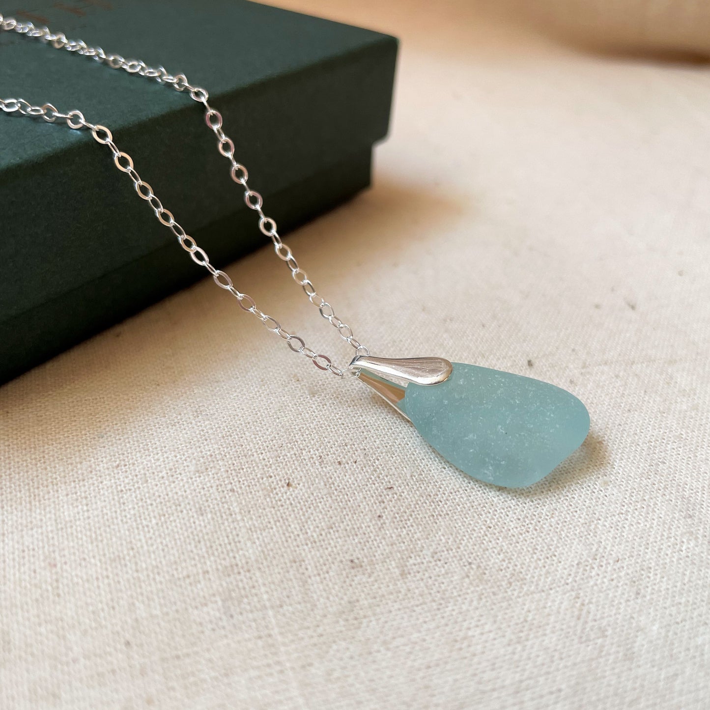 Blue sea glass necklace on silver chain hanging over a dark green gift box
