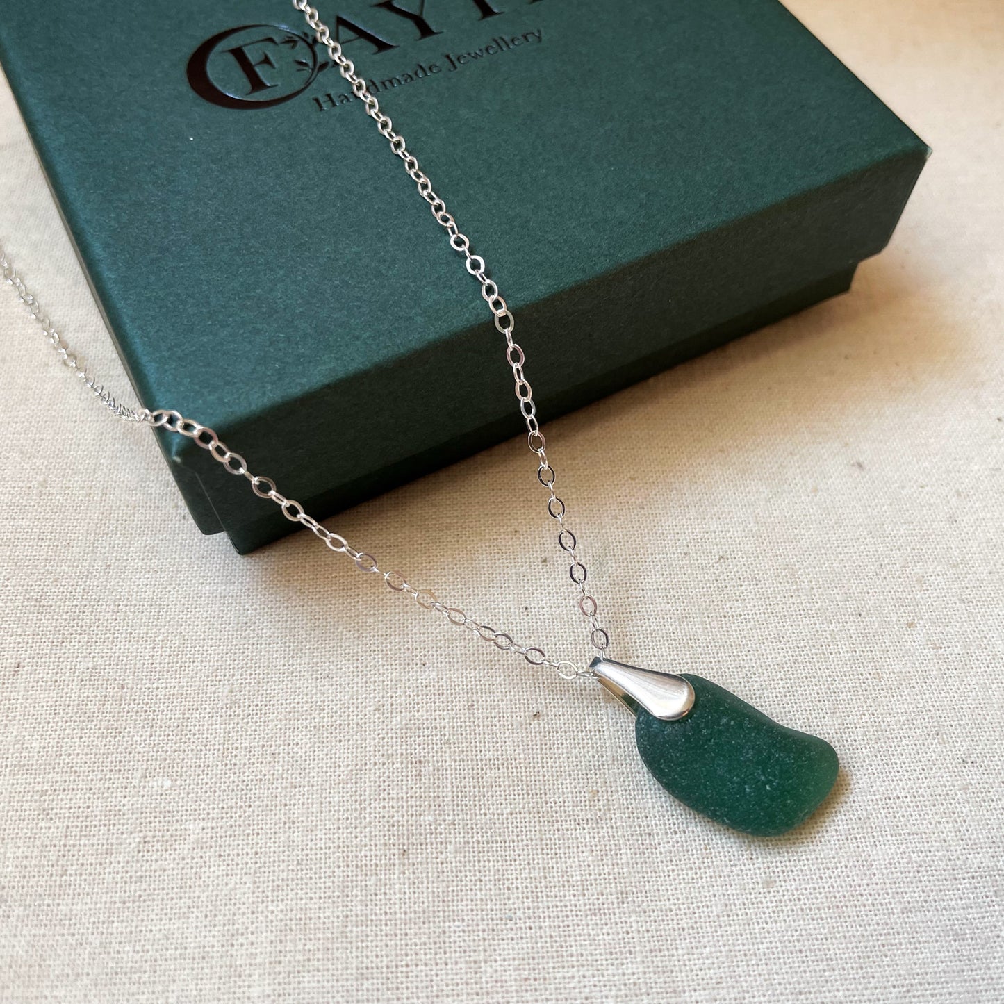 Green sea glass necklace on silver chain hanging over a dark green gift box