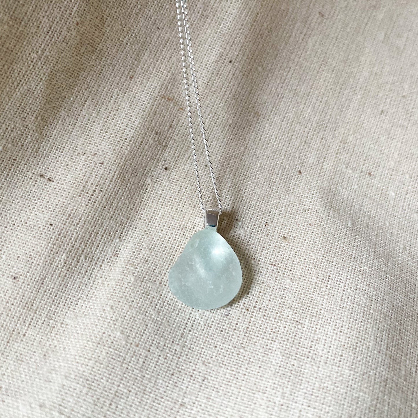 very pale blue sea glass necklace on beige background