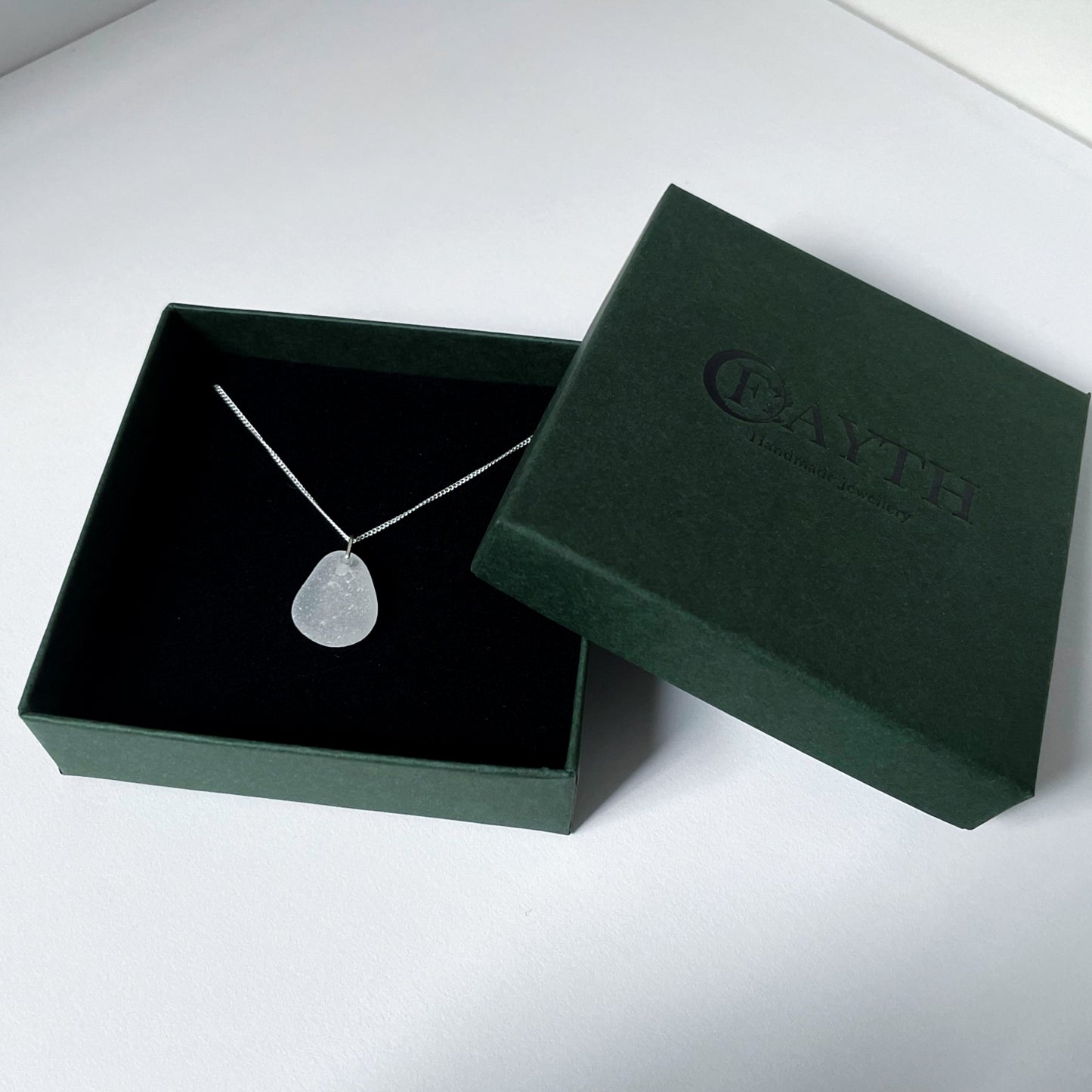 white sea glass necklace in gift box. Gift box is dark green with black foam.