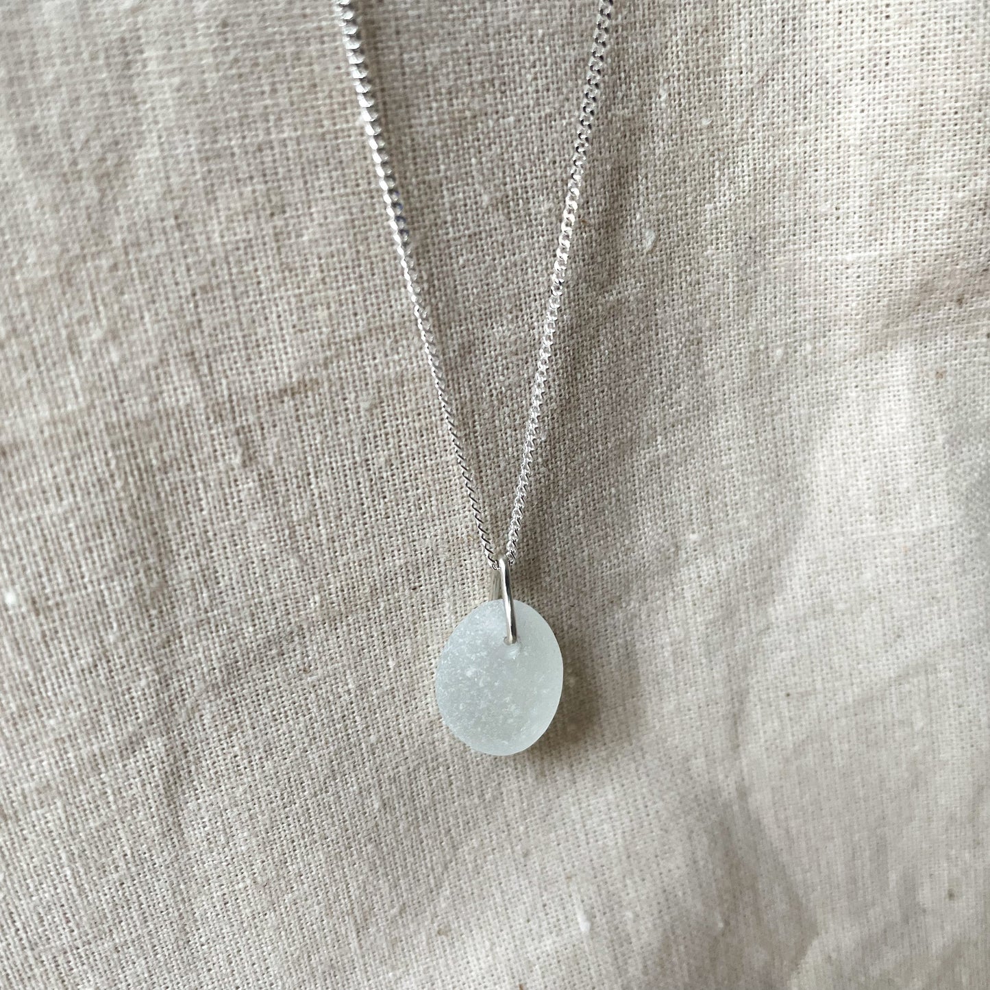 White sea glass and sterling silver necklace hanging against a beige background