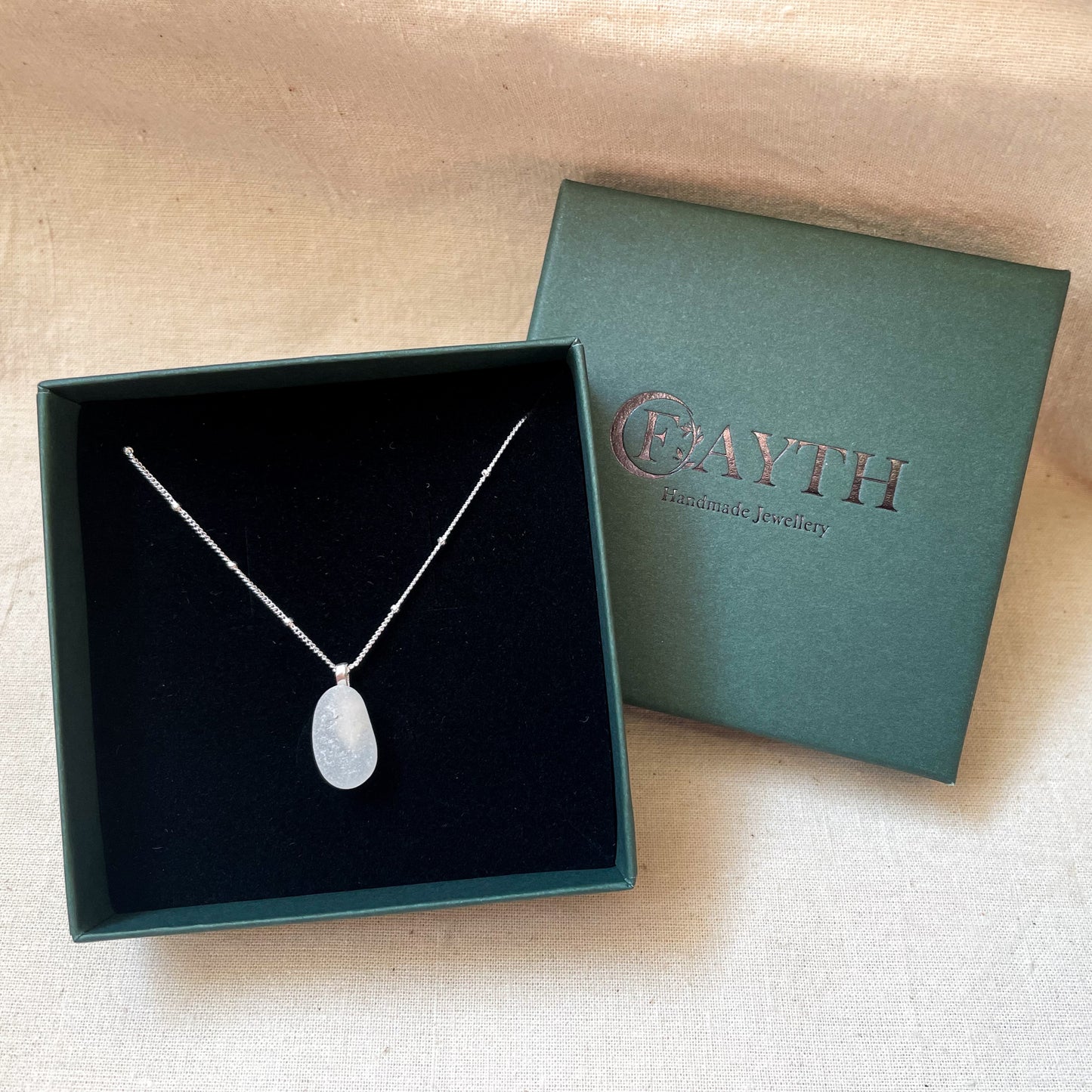 White sea glass necklace on a silver satellite chain in a dark green gift box with black foam insert