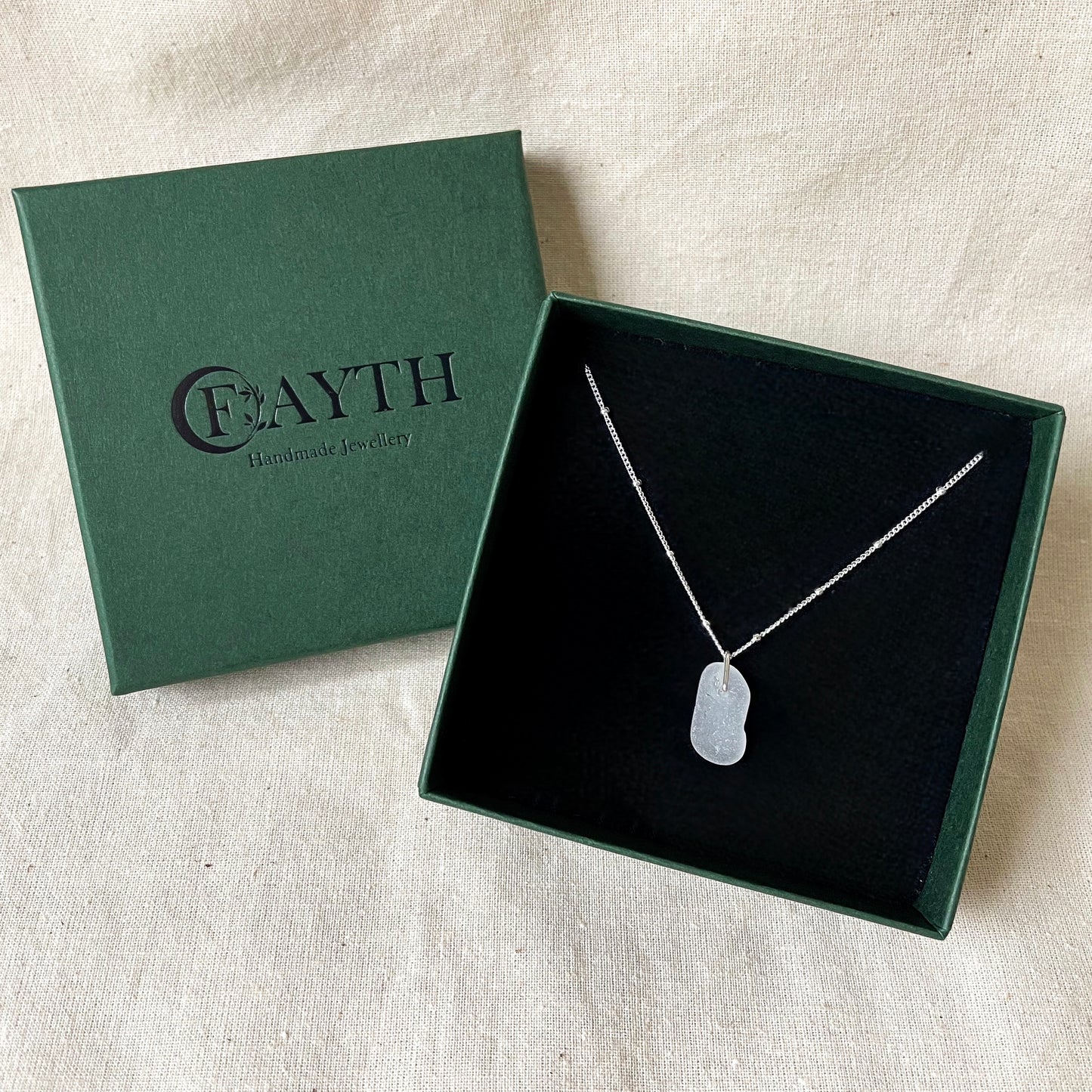 White sea glass necklace on silver satellite chain in a dark green gift box with a black foam