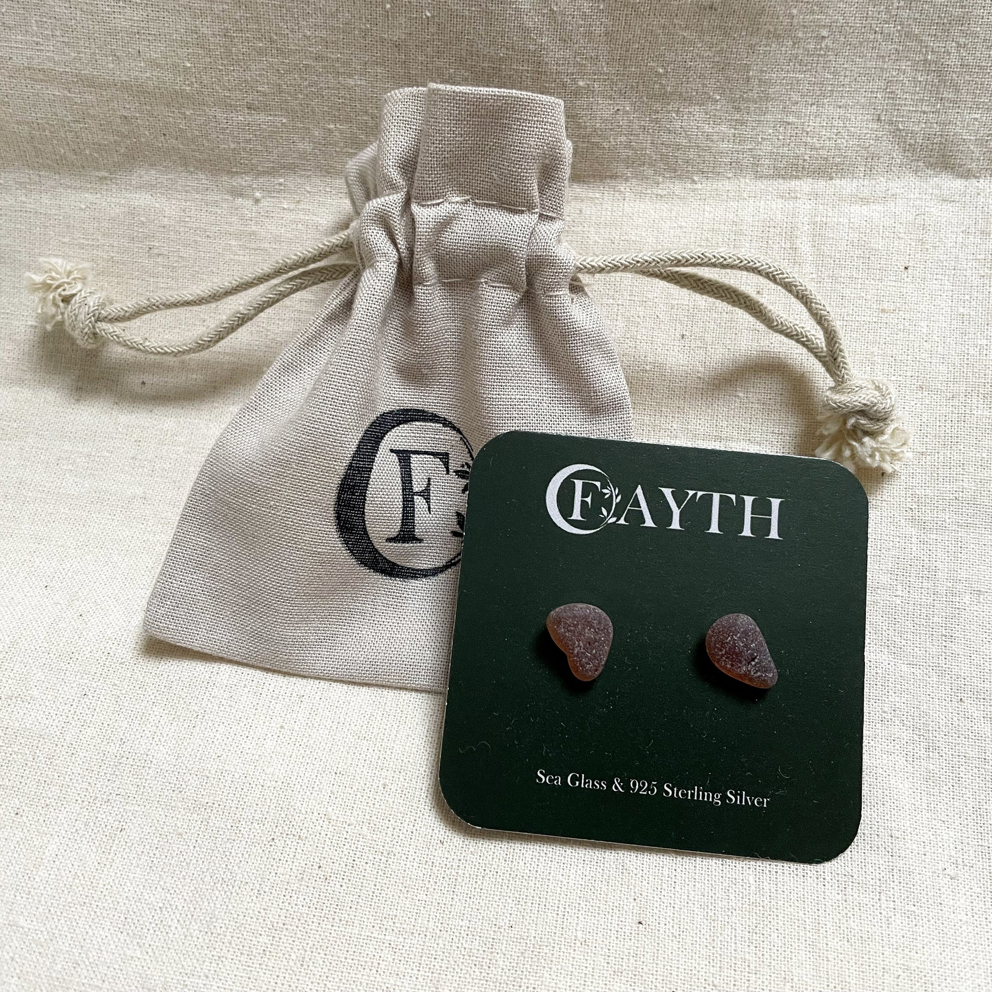 brown sea glass stud earrings on a dark green square branded display card against a beige branded cotton tie gift bag