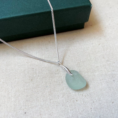 Light blue sea glass necklace on fine silver chain hanging over a dark green gift box