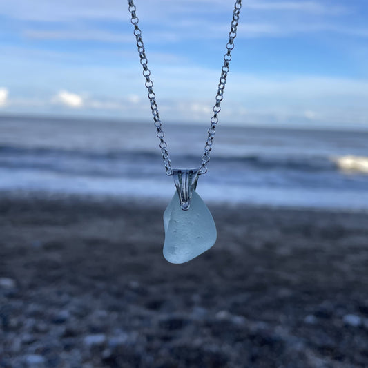 light blue seaglass necklace hanging in front of a blurred background of the sea.