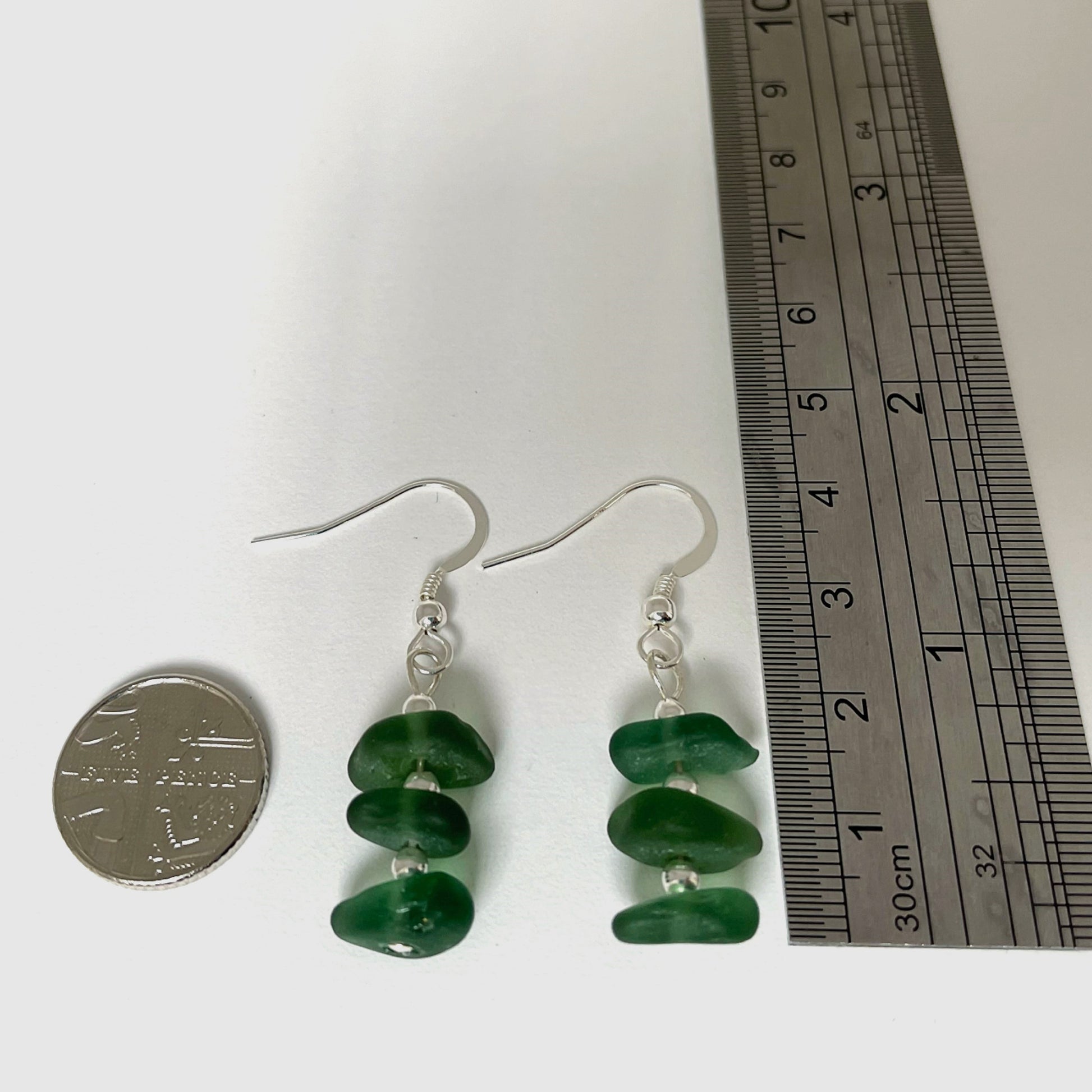 green sea glass and silver bead dangle earring laid down next to a 5 pence coin (left) and ruler (right) to show the size. earring approx. 4cm in height and about half width of the coin.