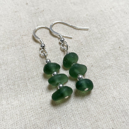 green sea glass earrings made up of three small pieces of green sea glass with three small silver beads in between, attached to a silver ear wire with a bead on