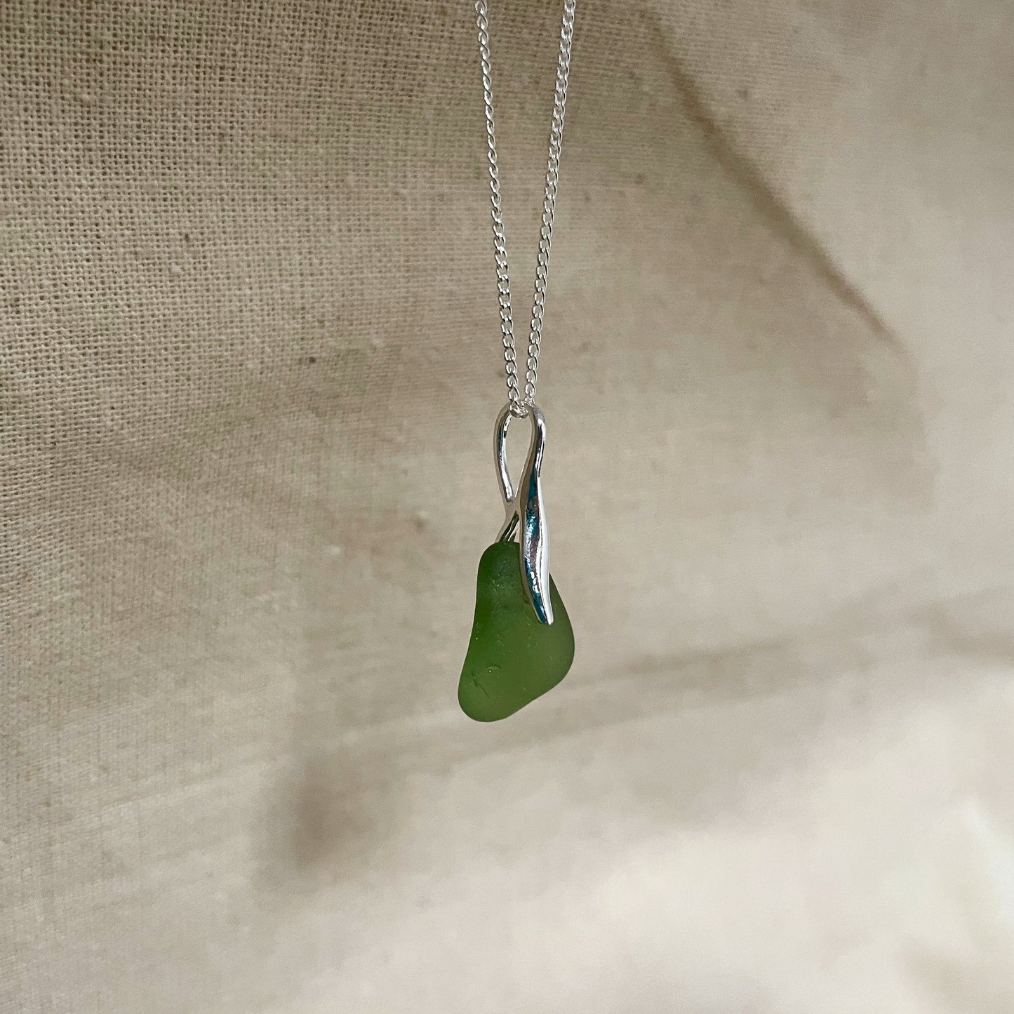 Green sea glass necklace hanging against a beige background