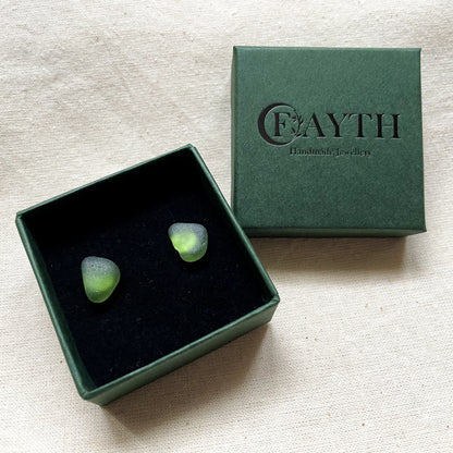 Green sea glass studs in a small dark green branded gift box with black foam inside 