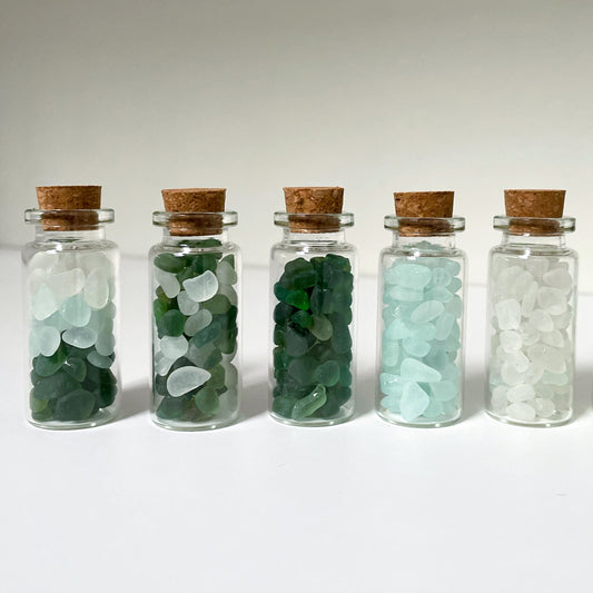 five small glass bottles with cork lids filled with mini pieces of sea glass in various colours