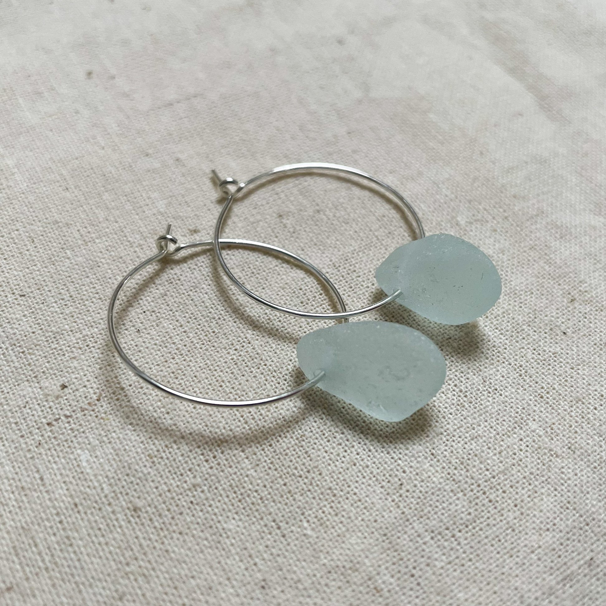 Silver hoop earrings with light blue sea glass.