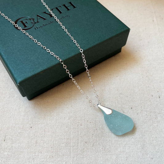 Blue sea glass necklace on silver chain hanging over a dark green gift box