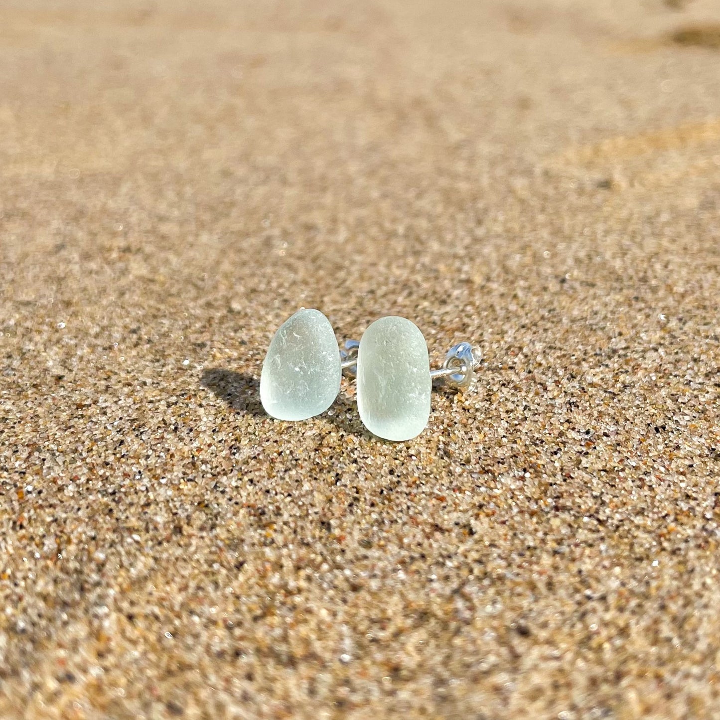 light blue sea glass studs on sand at the beach