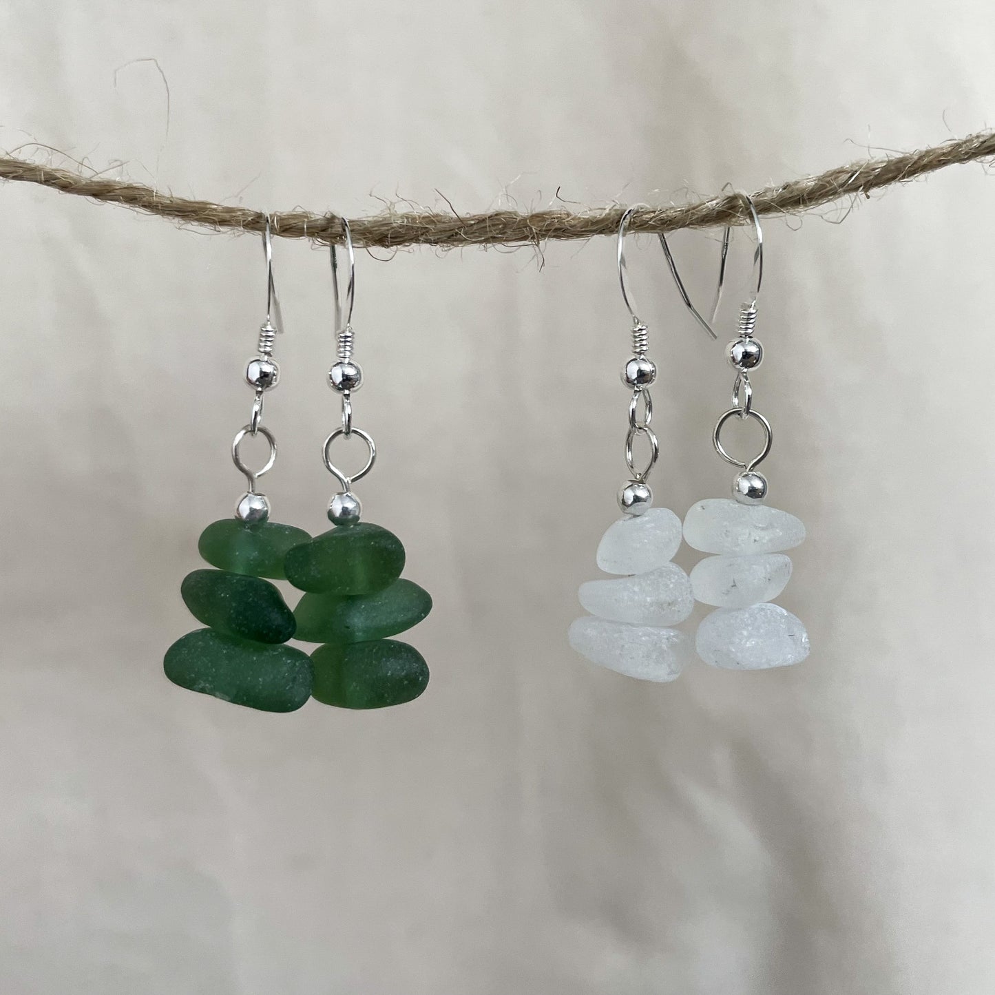 two pairs of earrings made out of sea glass and sterling silver, on the left a pair made from green sea glass and on the right a pair made from white sea glass