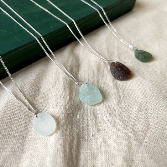 Four sea glass necklaces on fine sterling silver chains. White sea glass necklace (left), light blue sea glass necklace (middle), brown sea glass necklace (middle) and green sea glass necklace (right)