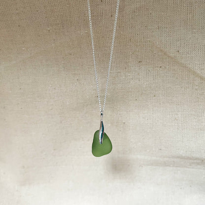 Green sea glass and sterling silver necklace hanging against a beige background