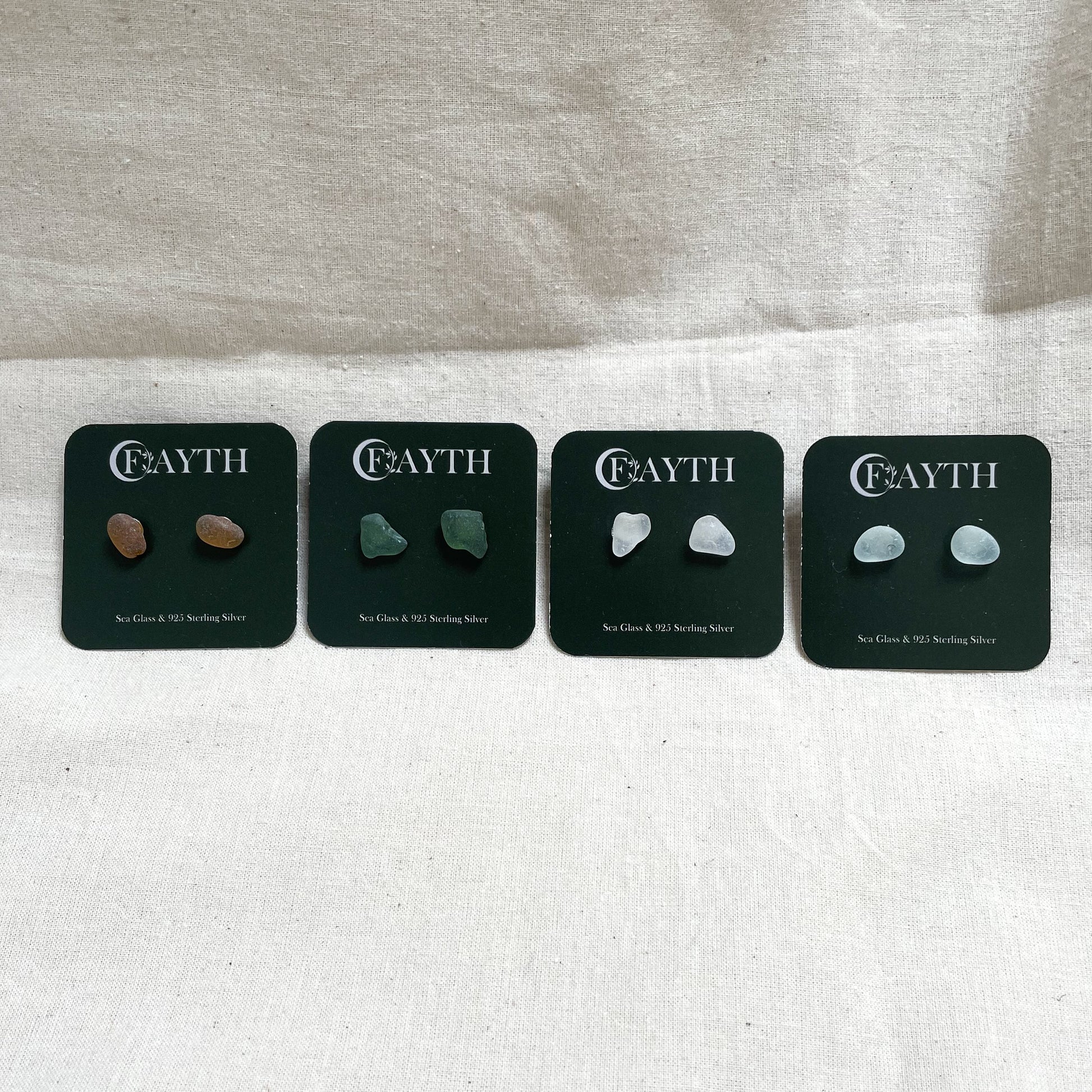 Four pairs of sea glass stud earrings on square dark green branded display cards in yellow (left), green (middle), white (middle) & light blue (right)