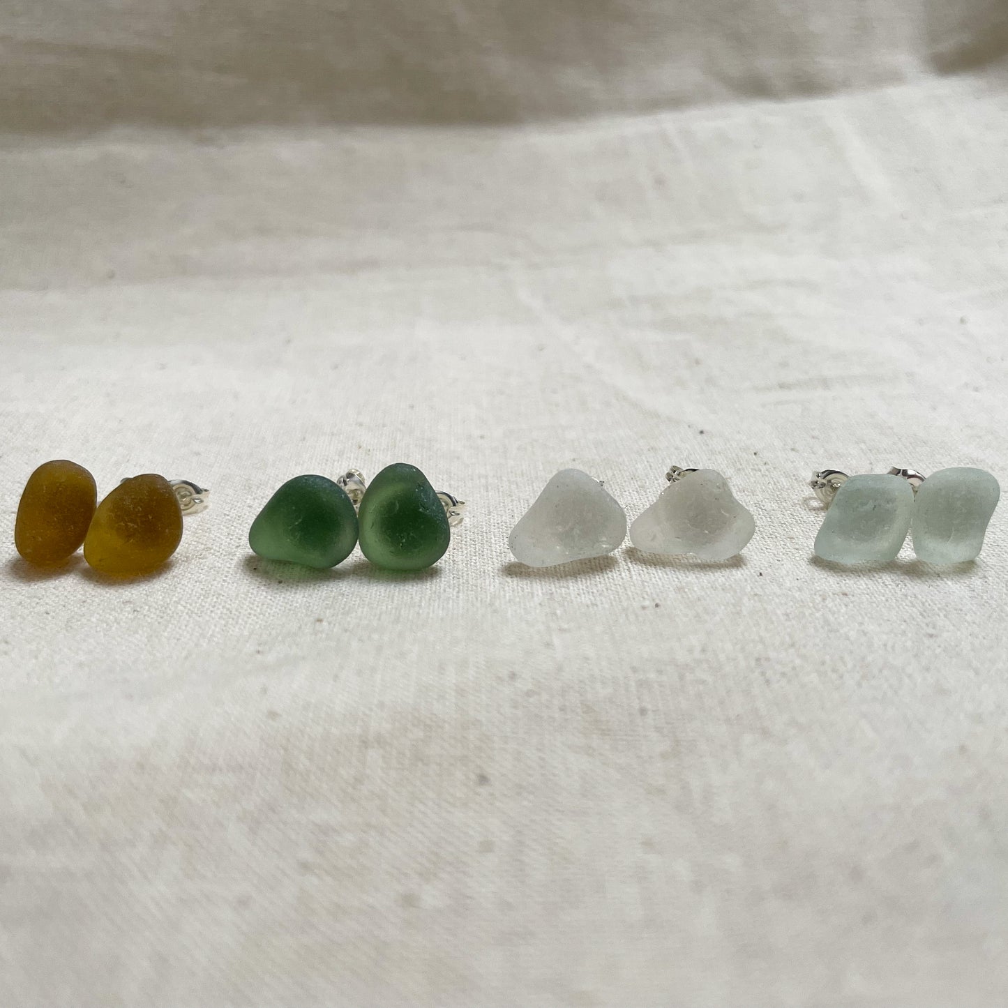 four pairs of sea glass stud earrings in yellow (left), green (middle), white (middle) & light blue (right)