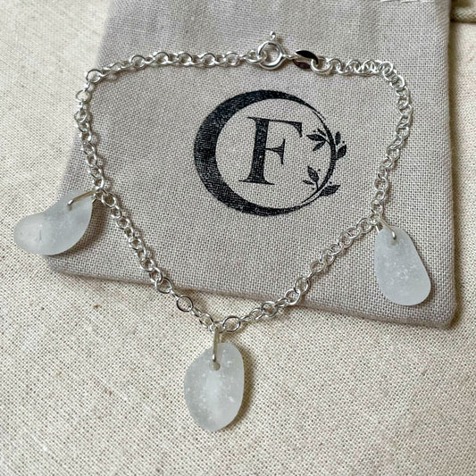 Sterling silver cable chain bracelet with three pieces of white sea glass on branded beige cotton gift bag.