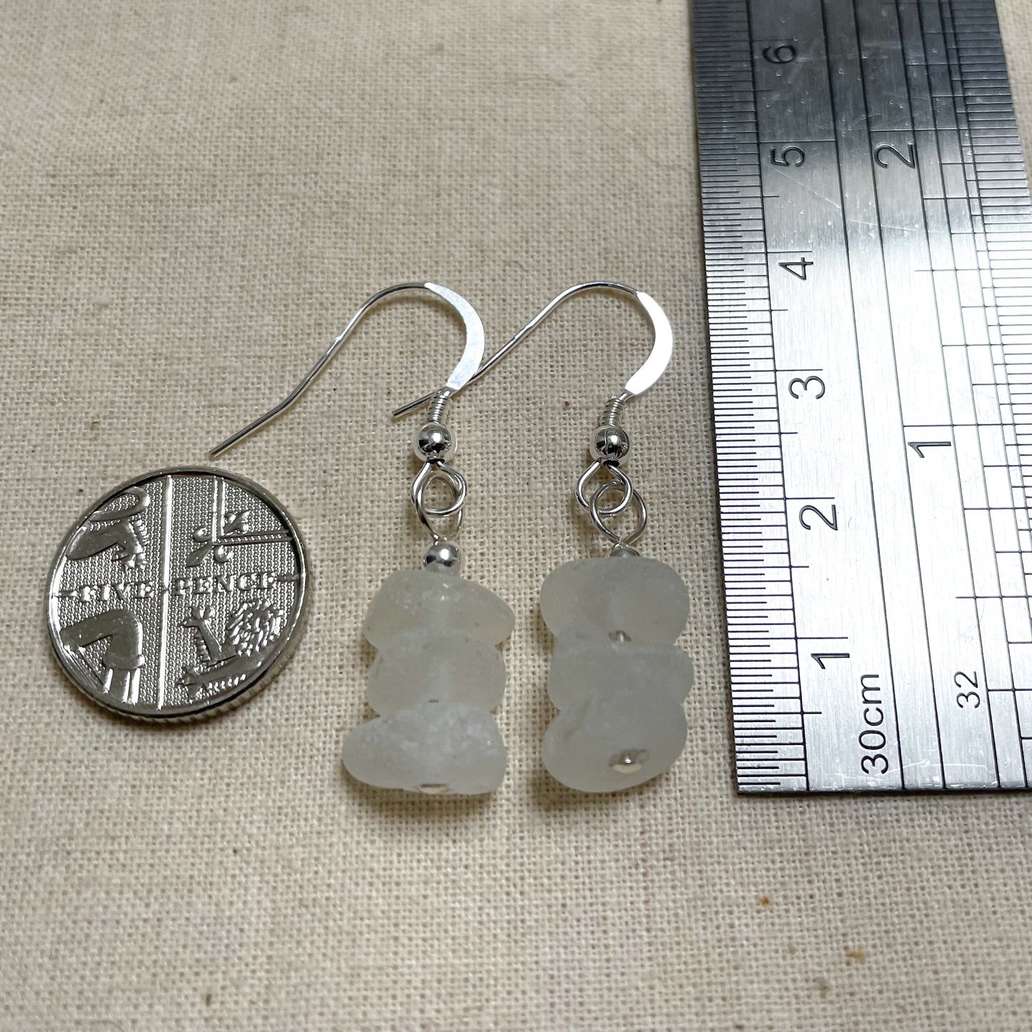 white sea glass earrings next to a ruler showing the height to be roughly 3.5cm and a 5 pence coin on the left showing the earrings are about half the width of the coin