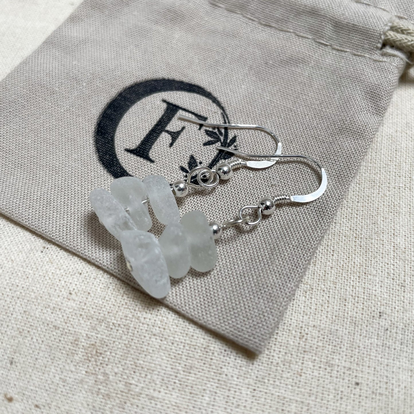 white seaglass earrings on a beige/grey cotton gift bag