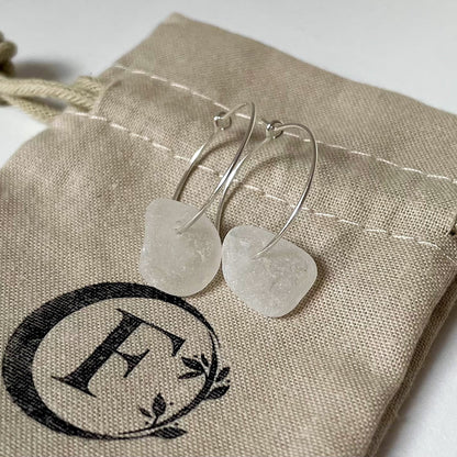 Silver hoop earrings with White sea glass are laid on a beige cotton tie bag