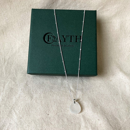 White sea glass necklace on silver satellite chain hanging over dark green gift box