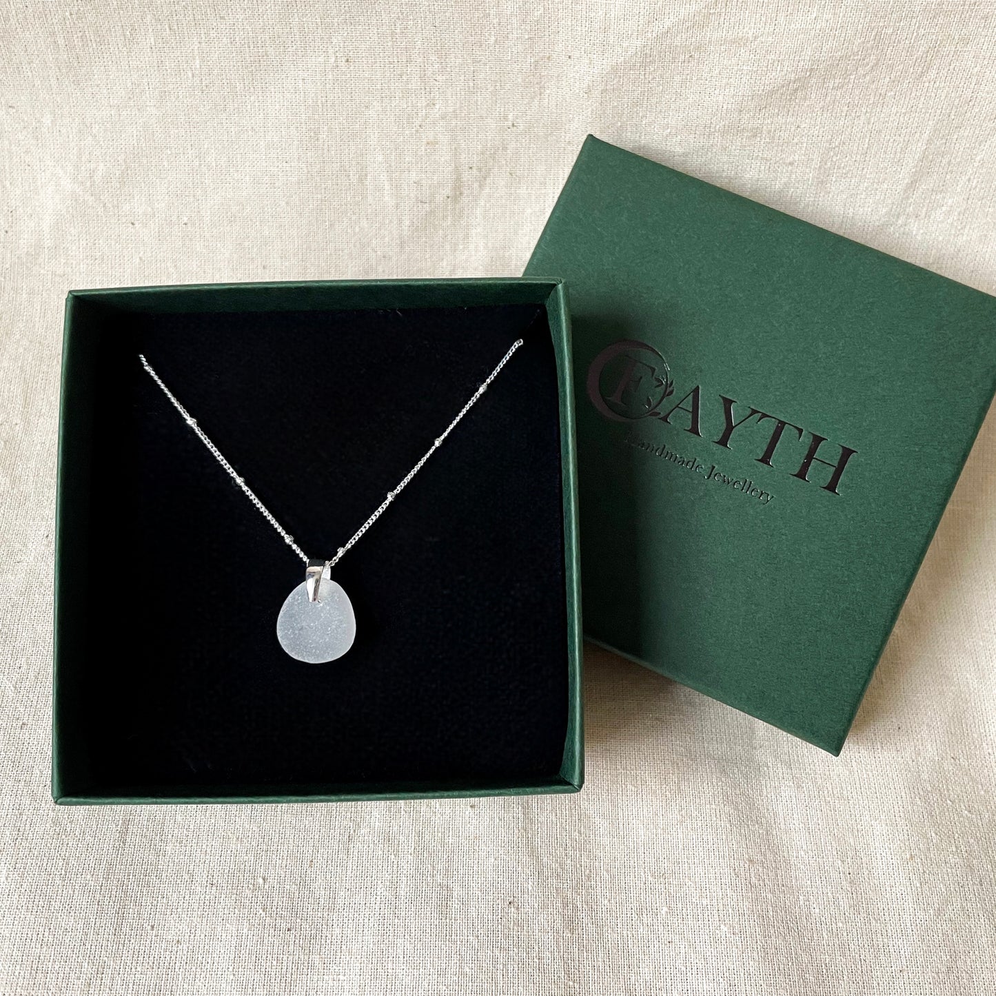 White sea glass necklace on silver satellite chain in a dark green gift box with a black foam inside